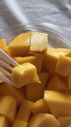 a glass bowl filled with sliced mangoes and two white plastic utensils in it