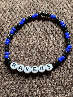 a blue and black beaded bracelet with the word raven's on it sitting on a carpet