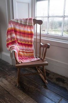 a rocking chair with a blanket on top of it in front of a large window