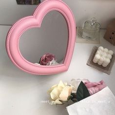 a pink heart shaped mirror sitting on top of a table next to flowers and candles