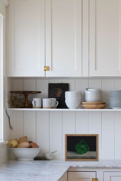 white kitchen cabinets and counter tops with dishes on the shelf above them in front of a window