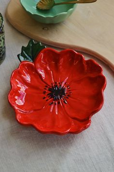 a red flower sitting on top of a table next to two bowls and spoons