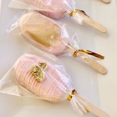 three pink and gold decorated cookies in plastic bags on top of a white countertop