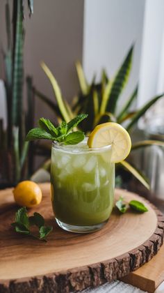 a green drink with lemon and mint garnish on a wooden tray next to potted plants