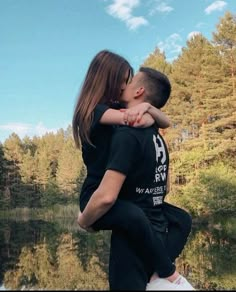 a man and woman are kissing in front of the water, with trees behind them