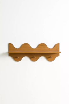 a wooden shelf mounted to the side of a wall with two hooks on each end