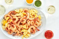 a white plate topped with shrimp and lemon wedges next to two cups of sauce