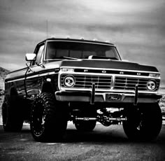 a black and white photo of an old pickup truck with big tires on the road