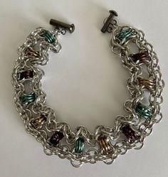 This chainmaille cuff measures 8.75 inches in length which will fit a wrist measuring between 7.75 and and 8.25 inches. The weave of the cuff is called byz band. The byzantine units have anodized aluminum rings in earthen colors of beige, brown and teal. These units are linked together with large and small shiny aluminum rings in a lacy finish to the bracelet. The colors of the bracelet pop out to give the impression of a studded cuff. The clasp is a gunmetal side locking tube.  Custom orders accepted on this bracelet. Metal Chainmail Bracelets As Gift, Metal Bracelets With Jump Ring For Jewelry Making, Metal Chainmail Bracelet, Earth Colors, Earth Color, Anodized Aluminum, Pop Out, Beige Brown, Chain Link Bracelet