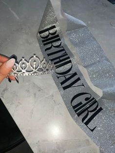 someone holding a tiara in their hand with the word happy birthday on it and silver ribbon