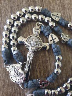 https://www.scapulars-au.com This is one of Our most popular Men's 5 Decade Rosary.  550 Military Charcoal Grey Paracord Rosary. 10 mm Stainless Steel Beads.  Crusader Jerusalem Shields on Our Father/Glory Be Beads. Stunning Silver Plated Italian Saint Benedict Crucifix valued at $24.95. Saint Michael Shield Centerpiece. Durable and made to last. Rosary For Men, Silver Rosary With Black Beads As Gift, Mens Rosary Necklace, Adjustable Black Spiritual Rosary, Combat Rosary, Silver Rosary With Black Beads And Crucifix, Mens Rosary, Paracord Rosary, Mens Silver Necklace