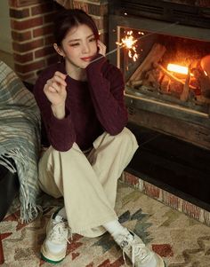 a woman sitting on the floor in front of a fire place with her hand up to her face