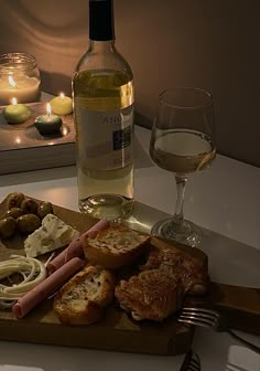 a bottle of wine and some food on a wooden tray with a candle in the background