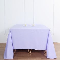 a table with two candles on it in front of a white wall and wood floor