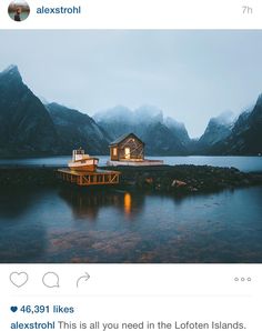 a small cabin sits on the edge of a body of water with mountains in the background