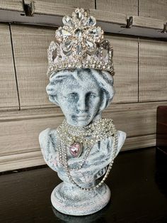 Add a touch of elegance to your space with our hand-painted Bust Statue with Crown. Available in silver or gold accents, each bust features rhinestones and a unique neck piece. The removable hand made metal crown is adorned with more rhinestones for a regal look. Made of poly resin and perfect for any home or office setting. Silver Crown -This bust has silver accents. She has rhinestones and a pink heart around her neck. Her metal crown is hand made, removable and is painted white and black with Bohemian Crown Shaped Jewelry Gift, Crown Canvas White, Crown Sculpture Statues, Silver Crown-shaped Metal Jewelry, Glamorous Crown-shaped Rhinestone Jewelry, Pink Heart Necklace, Metal Crown, Silver Crown, Gold Crown