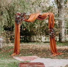 an outdoor ceremony with orange draping and floral arrangements on the altar, along with rugs