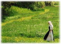 a woman is walking in the grass with a white veil on her head and black dress