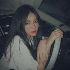 a woman sitting in the driver's seat of a car with her hand on the steering wheel