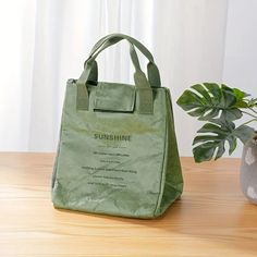 a green bag sitting on top of a wooden table next to a potted plant