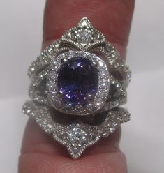 a close up of a person's hand holding a ring with a purple stone in it