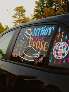 the side window of a car decorated with colorful stickers and writing that says senior only goose