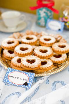 a table topped with lots of cookies on top of a metal plate next to a cup and saucer