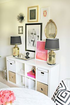 a white table topped with lots of drawers next to a lamp and pictures on the wall