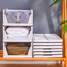 a wooden shelf with clothes and folded shirts on it next to a potted plant