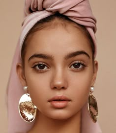 a young woman wearing large gold earrings and a pink head scarf is looking at the camera