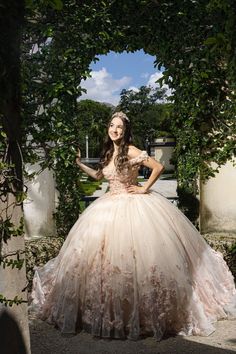 a woman in a ball gown standing under an arch with her hands on her hips