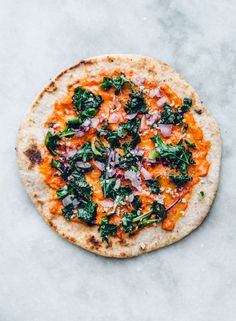 a flat bread pizza topped with spinach and red onions on a marble countertop