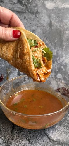 a hand holding a piece of food over a bowl of soup and dipping sauce on the side