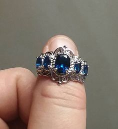 This lovely ring is a showstopper with Victorian flair. With four 5x3mm lab created sapphires, and a beautiful 8x6mm lab created sapphire centerstone, surrounded by curls and filigree, it is a beautiful piece to see in the sun. This ring is 925 sterling silver and is rhodium plated for lasting shine US size 7. Elegant Sapphire Filigree Ring In Oval Shape, Elegant Sapphire Oval Filigree Ring, Elegant Sapphire Filigree Ring With Oval Shape, Elegant Oval Sapphire Filigree Ring, Garnet Gem, Lovely Ring, Multi Stone Ring, Multi Stone, Stone Rings