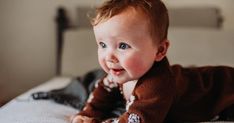 a smiling baby laying on top of a bed