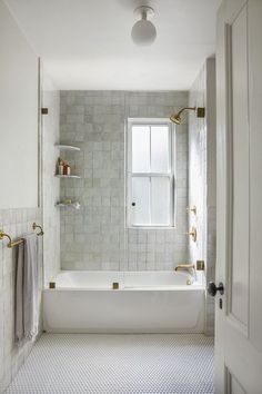 a bathroom with white tile and gold fixtures, including a bathtub in the corner