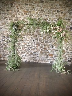 an arrangement of flowers and greenery on a stone wall in front of a wooden floor