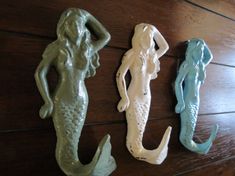 three ceramic mermaid figurines sitting on top of a wooden table