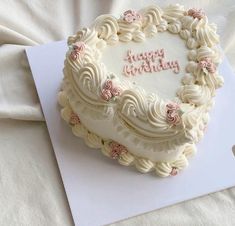 a birthday cake with white frosting and pink flowers on it sitting on top of a piece of paper