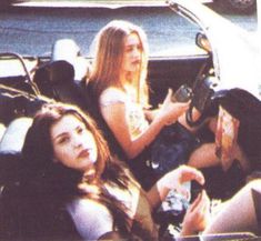 two young women sitting in the back of a car, one holding a cell phone