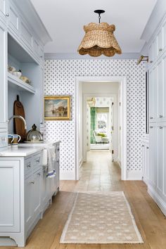 a hallway leading to a kitchen with white cabinets and patterned wallpaper on the walls