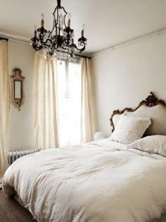 a white bed sitting under a window next to a chandelier