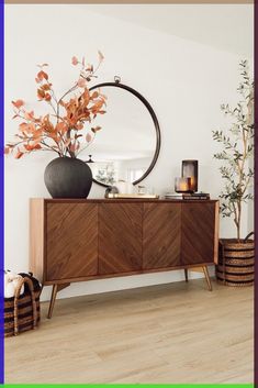 a room with a large mirror, vase and plants on the sideboard in front of it