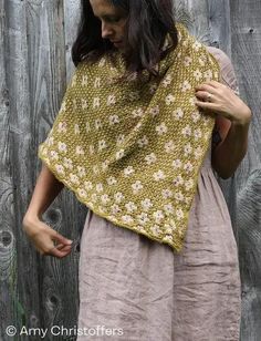 a woman wearing a shawl standing in front of a wooden fence with her hands on her hip