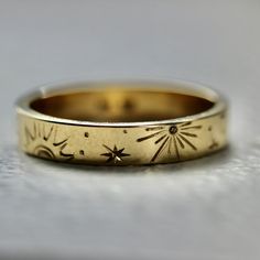 a gold wedding band with flowers and stars engraved on the side, sitting on a white surface