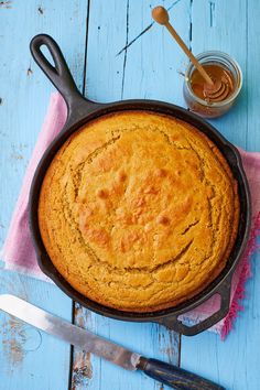 a cake in a cast iron skillet next to a knife and spoon on a blue wooden table