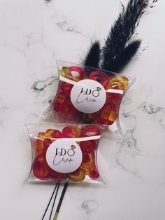 two bags filled with gummy bears sitting on top of a counter next to a black feather