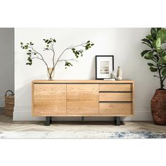 a wooden dresser sitting next to a potted plant on top of a rug in front of a white wall