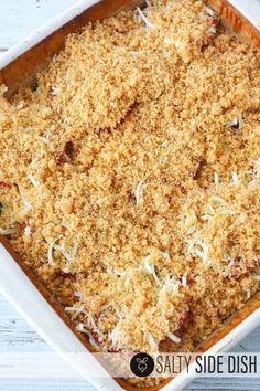 a casserole dish filled with meat and cheese crumbled on top, sitting on a white wooden table