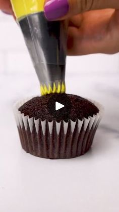 a cupcake being frosted with yellow icing by a person holding a knife